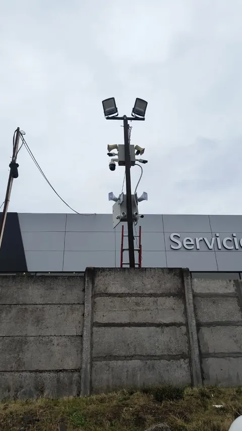Poste con cámaras y reflectores sobre el muro perimetral de una automotora