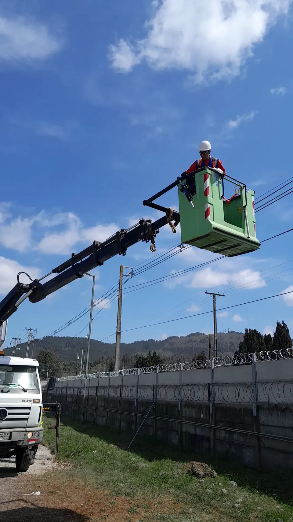 Técnico en un camión grúa instalando equipos de seguridad en un poste junto a un muro perimetral
